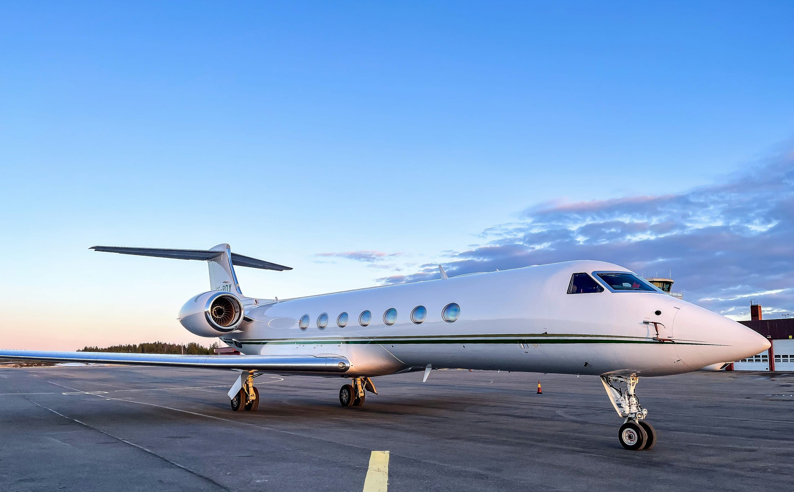 A private jet parked on the tarmac at dusk, with a colored sunset sky in the background